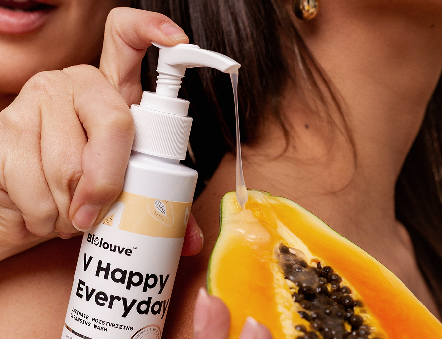 Hand holding Biolouve intimate spray next to halved papaya on warm background