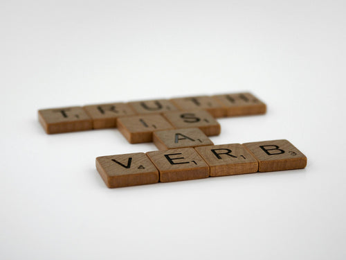 Wooden Scrabble letter tiles spelling Truth Is A Verb representing debunking intimate care myths