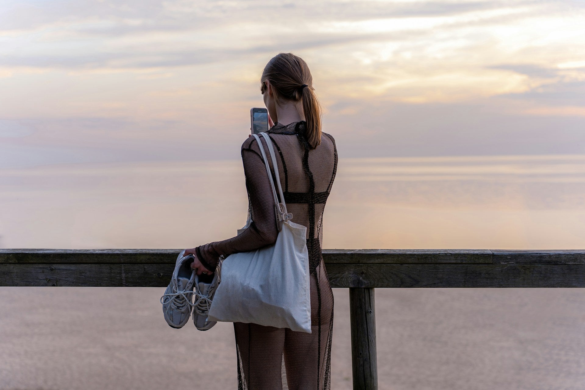 Woman in athletic wear holding gym bag and sneakers at sunset after workout
