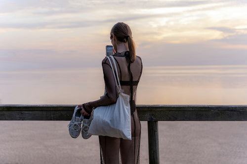 Woman in athletic wear holding gym bag and sneakers at sunset after workout