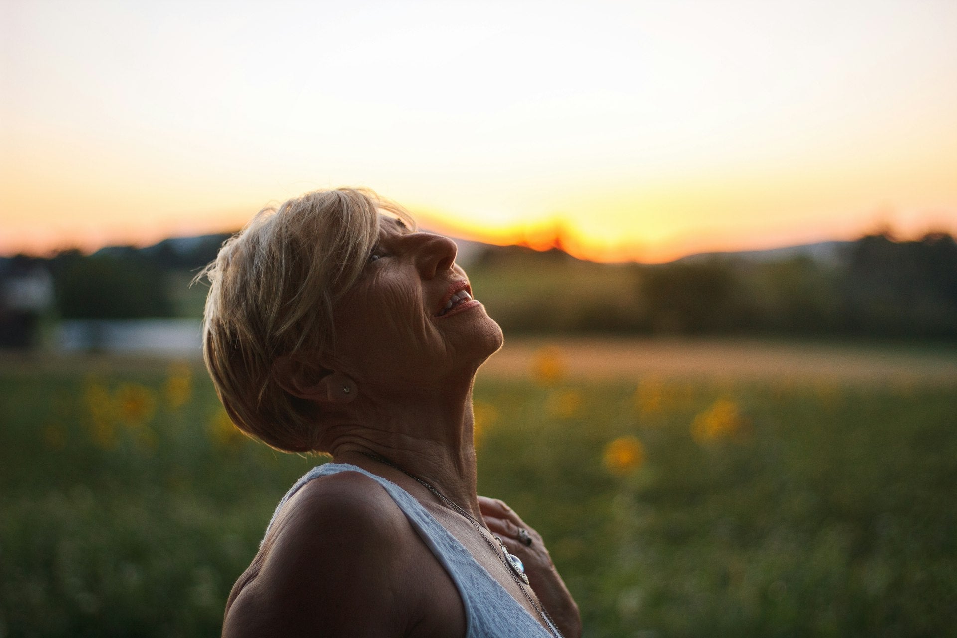Mature woman with short blonde hair breathing deeply in sunlit field at golden hour representing wellness at every age